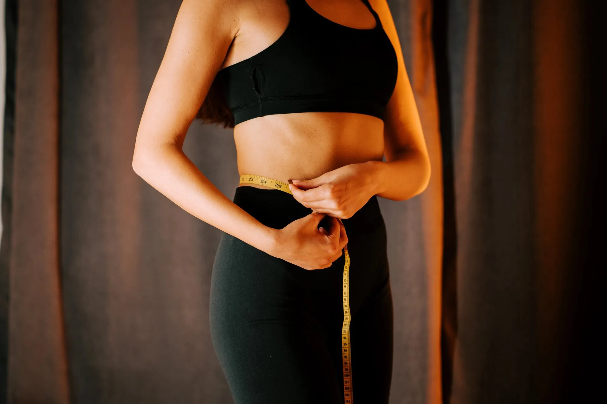 A woman in black measuring her waist.