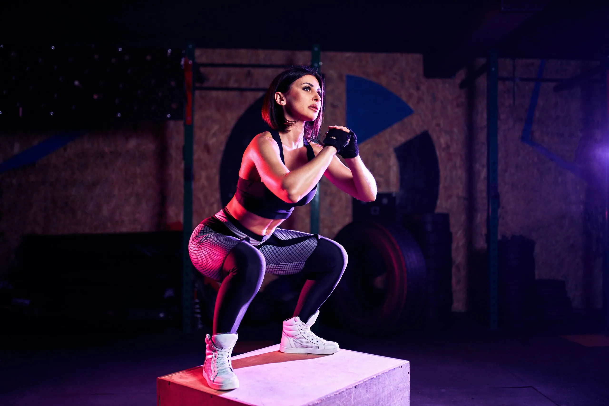 A woman in a black and grey outfit is squatting on a box.